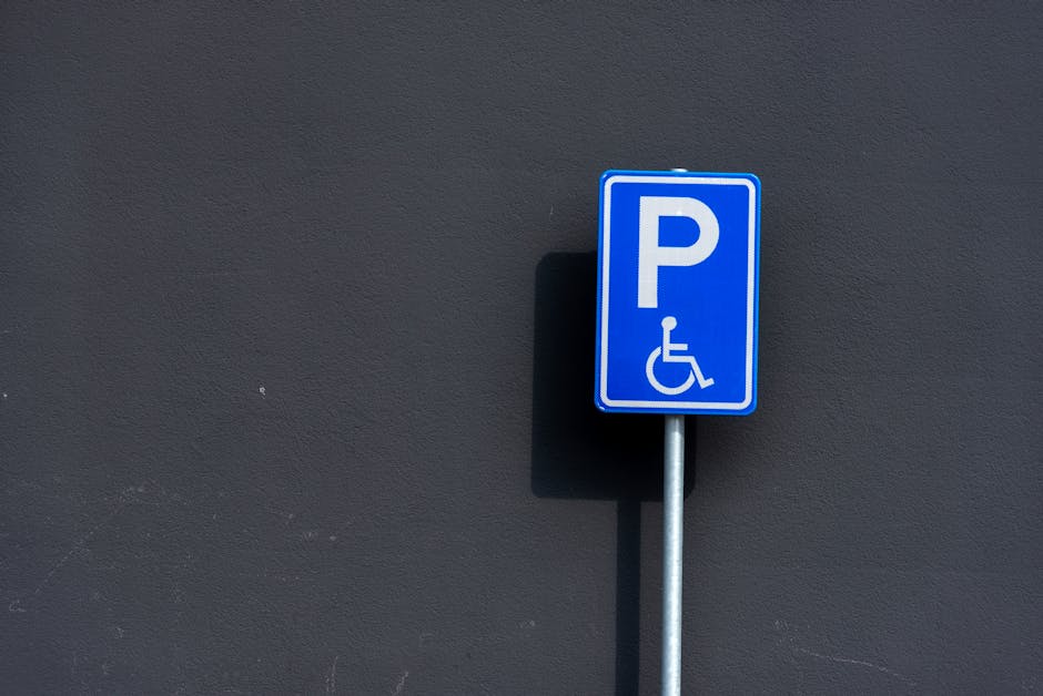 A rectangular white metal sign with bold black lettering reading 'NO PARKING DAY OR NIGHT' is mounted on a grey wooden door or garage door. The sign is attached with four screws, one at each corner. The door features horizontal and vertical panel details, and the surface has a smooth finish. The environment appears to be an outdoor or semi-outdoor setting, with natural lighting highlighting the sign and door surface. The sign's placement indicates a restriction on vehicle parking on the driveway or property frontage, which is relevant for residents and professional removal services like Man with Van Kingsbury when planning home relocation or furniture transport, especially during loading and unloading phases.